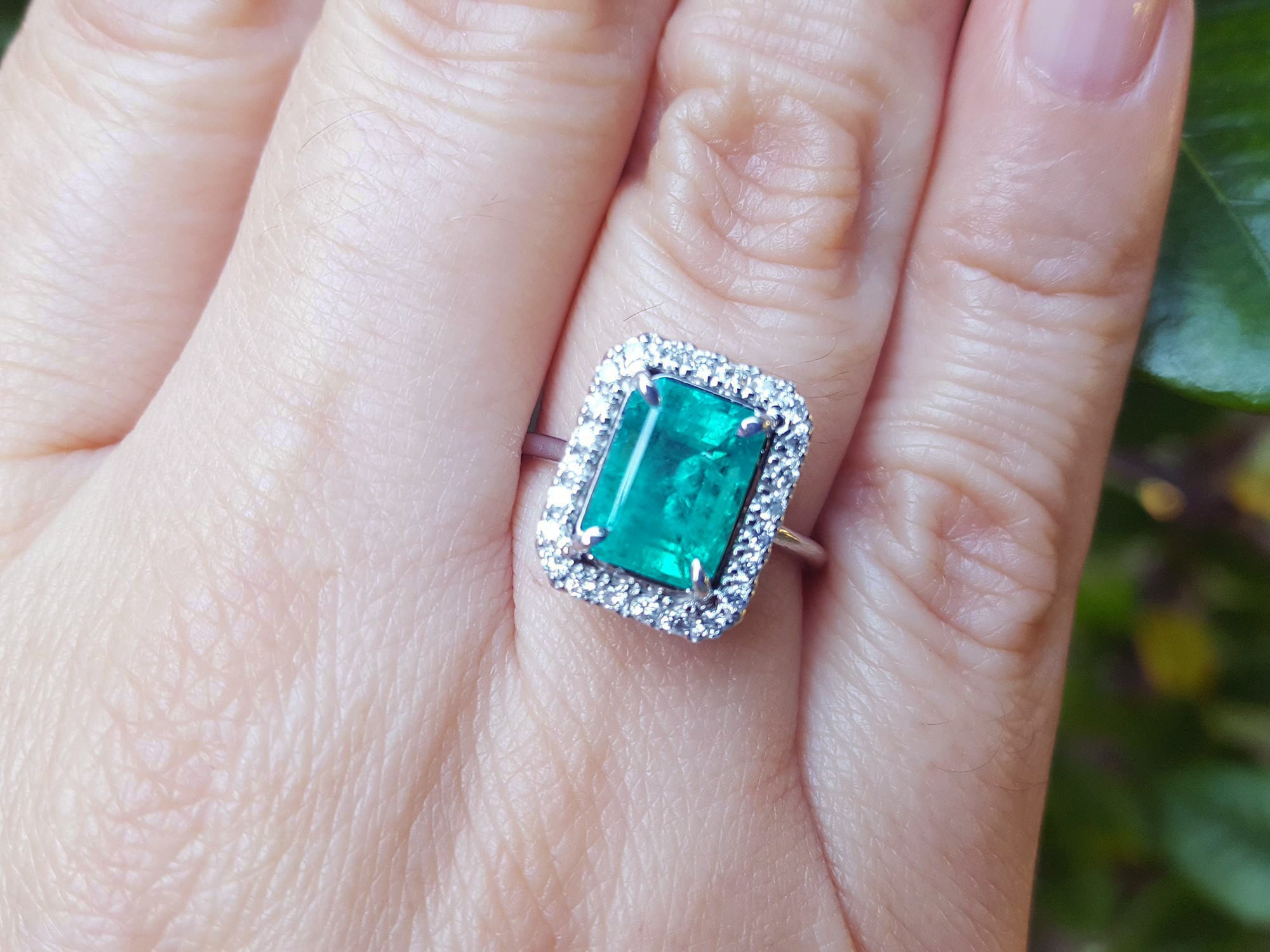 Emerald ring for women with halo diamond on a person's finger.