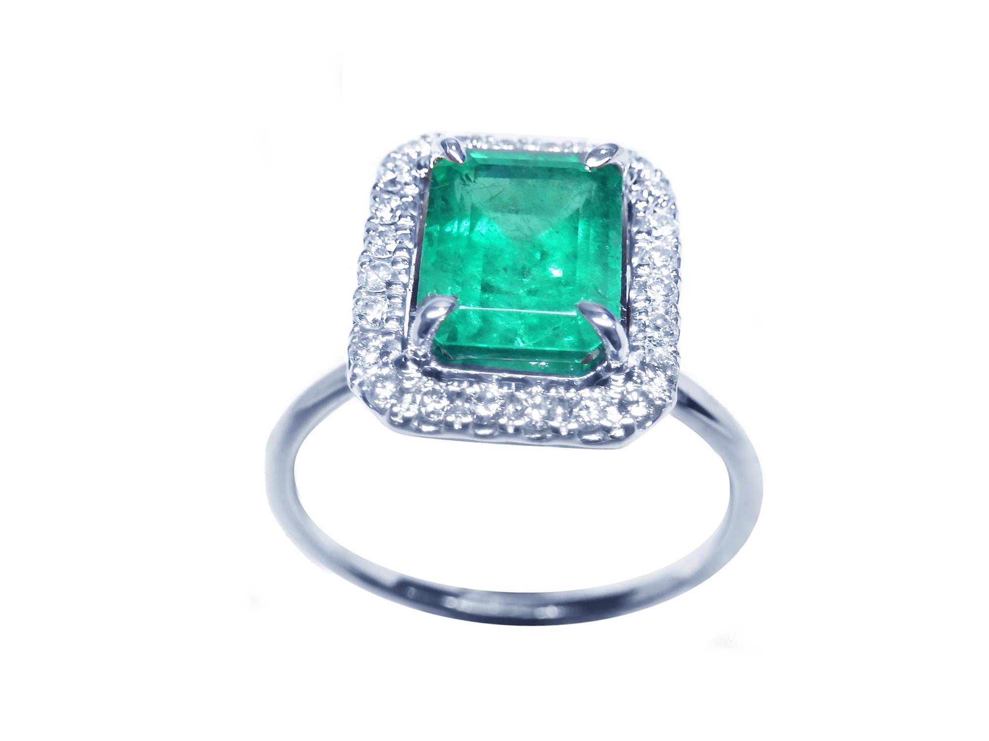 Ring with emerald and halo diamond in white gold on a white background.