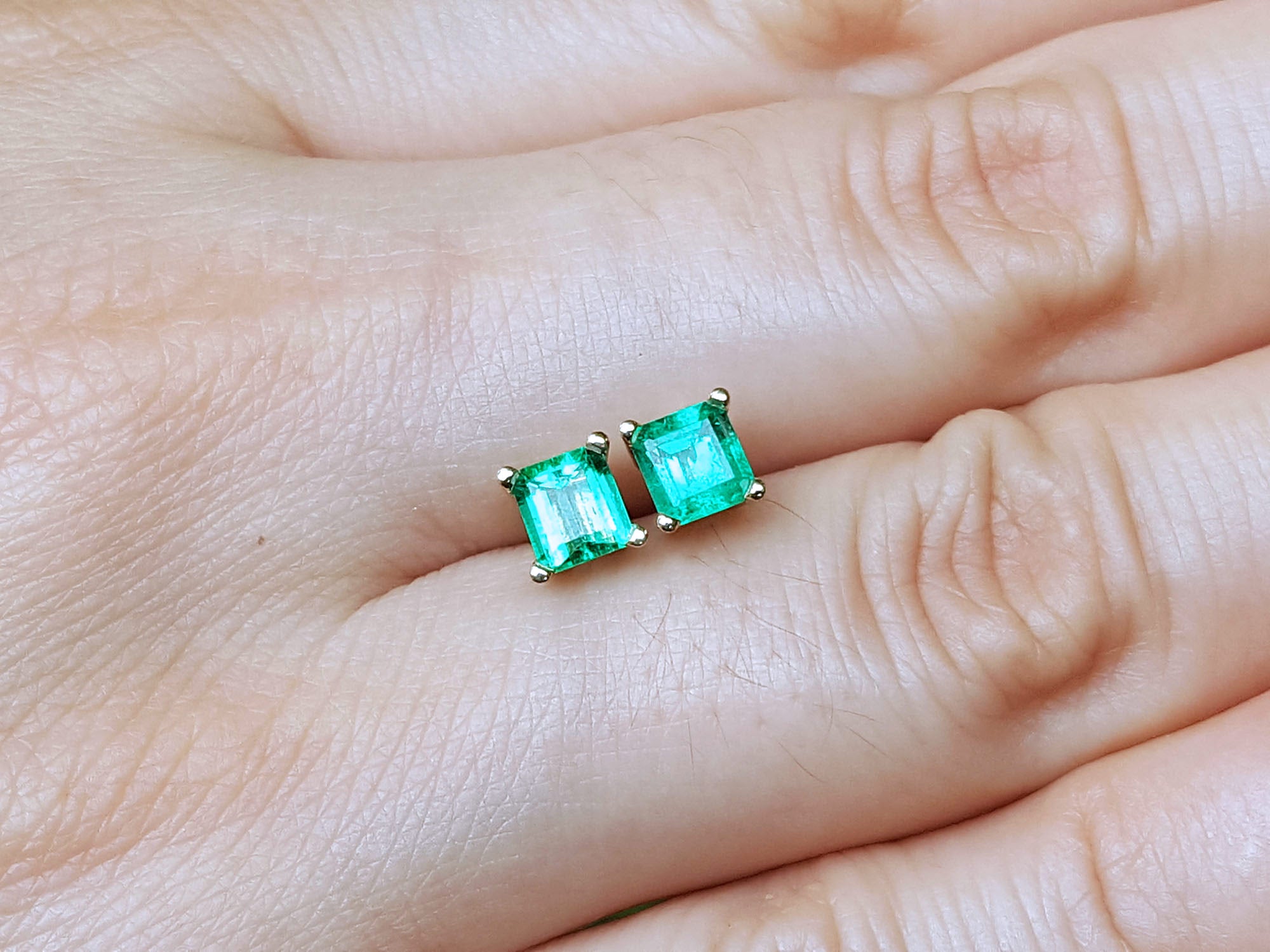 Genuine emerald stud earrings held between fingers.