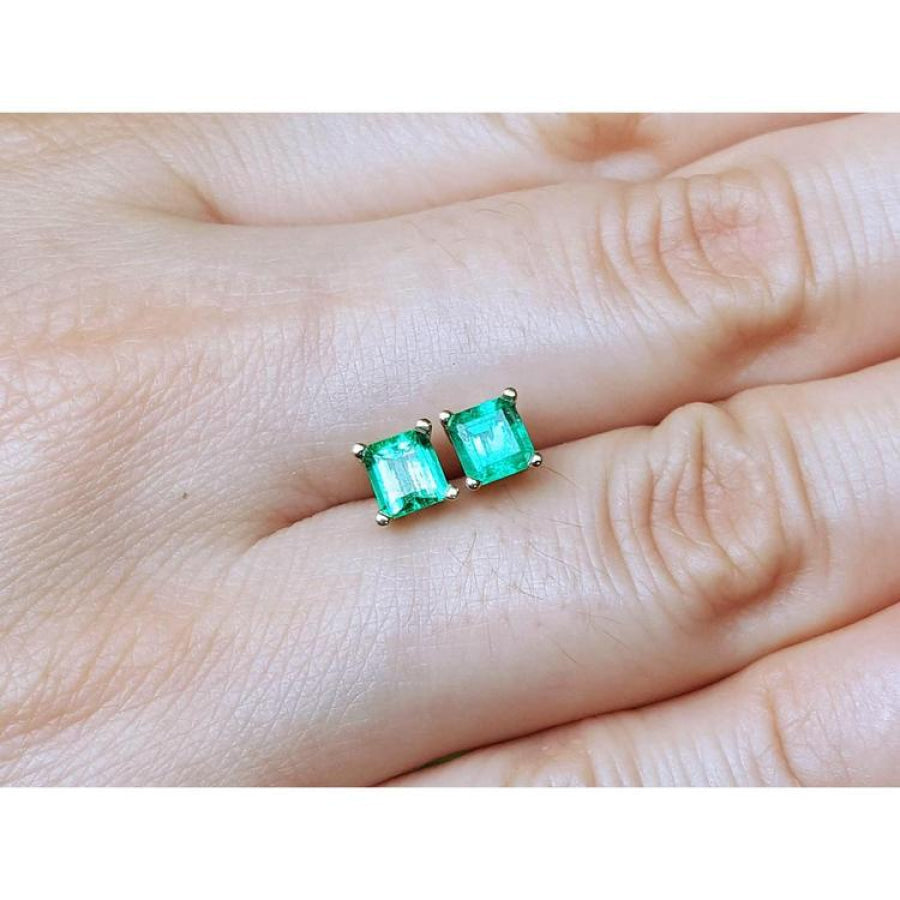 Pair of square emerald stud earrings in 14K yellow gold, worn on an earlobe.