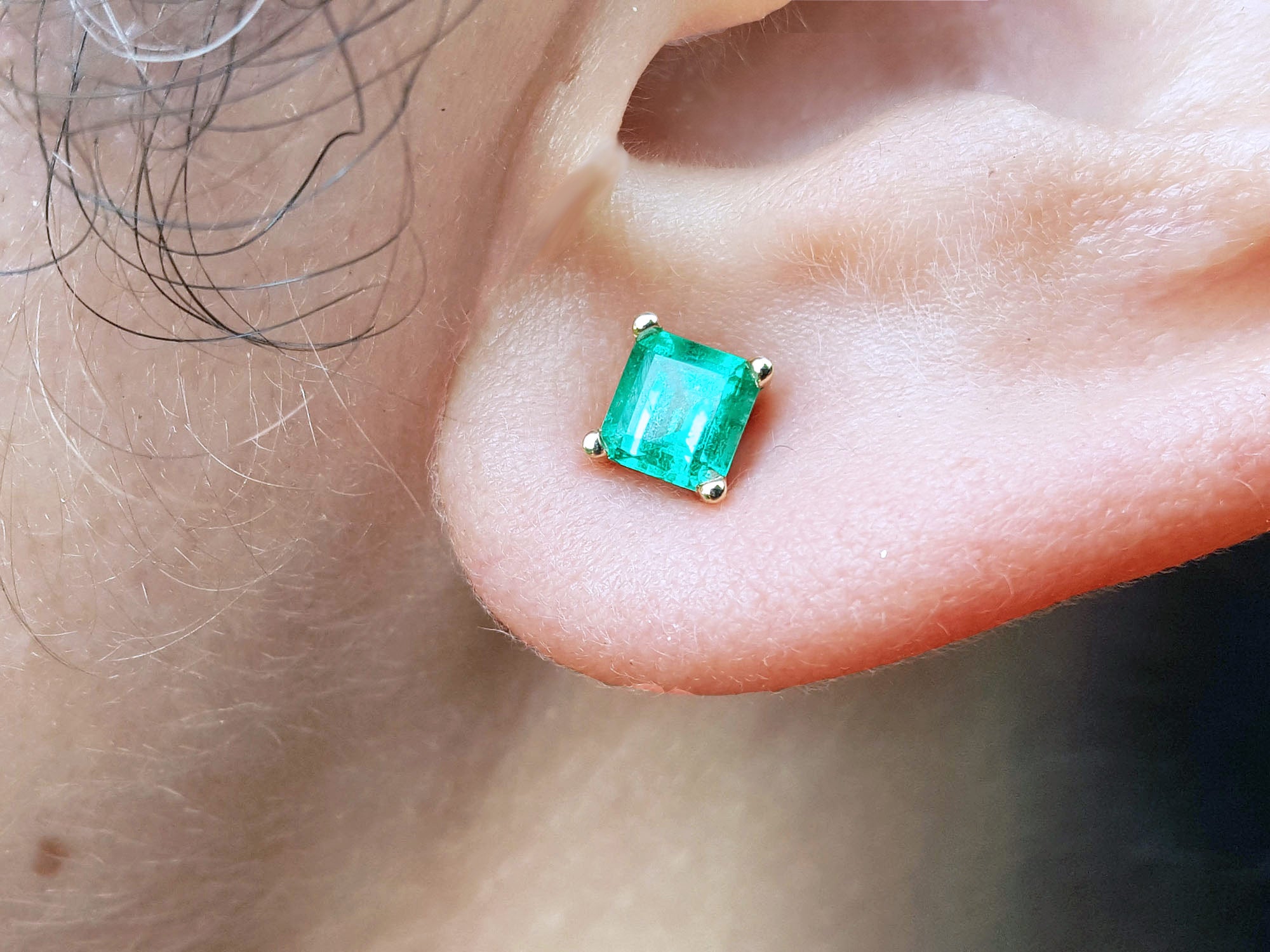 Square emerald stud earring on a person&#39;s ear.