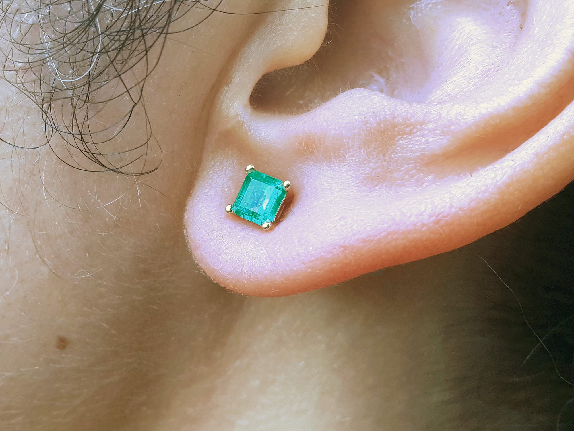 Close-up of an emerald gemstone earring on a person&#39;s ear.