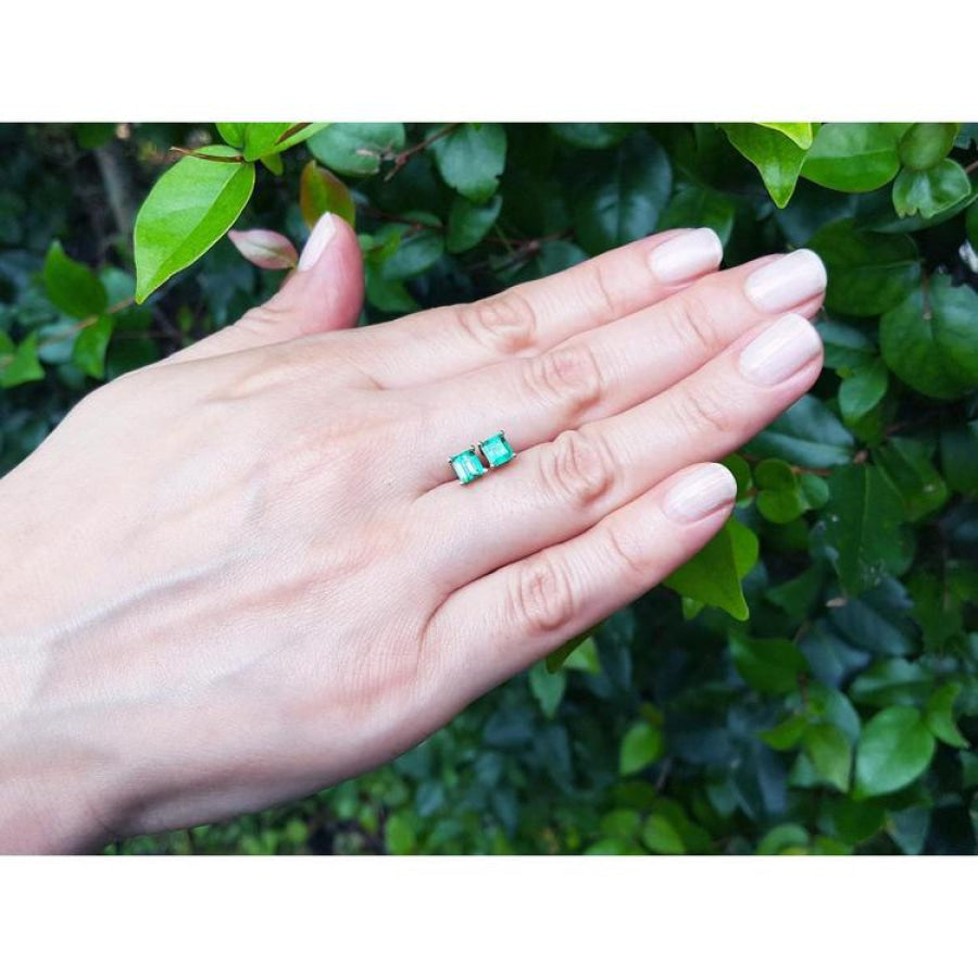 14K yellow gold square emerald stud earrings on a hand, surrounded by green leaves.