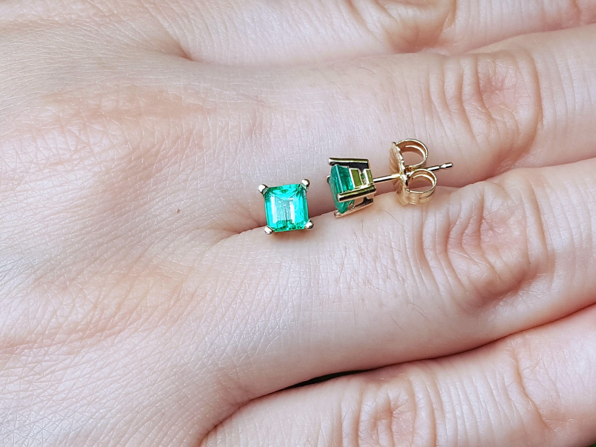 Square emerald stud earrings on a hand.