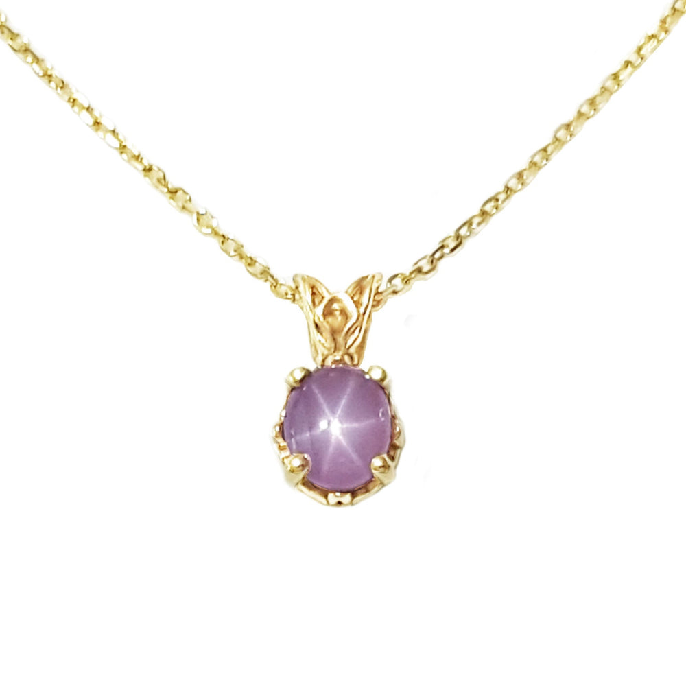 This natural star pink sapphire pendant necklace shows its asterisk under a LED bulb light and it is made of 14kgold.