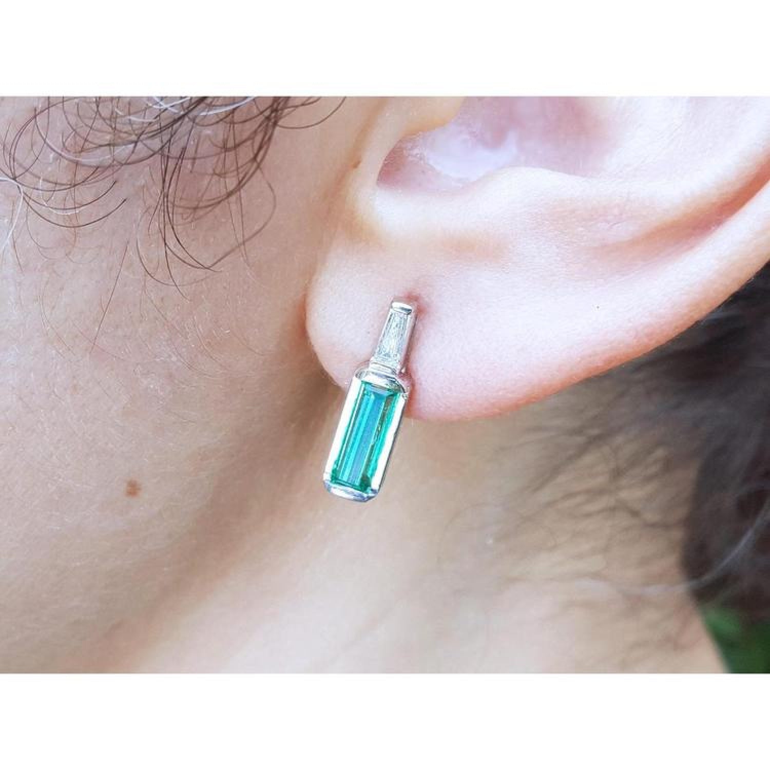 Baguette emerald and diamond stud earring in 14k white gold, worn on an ear.