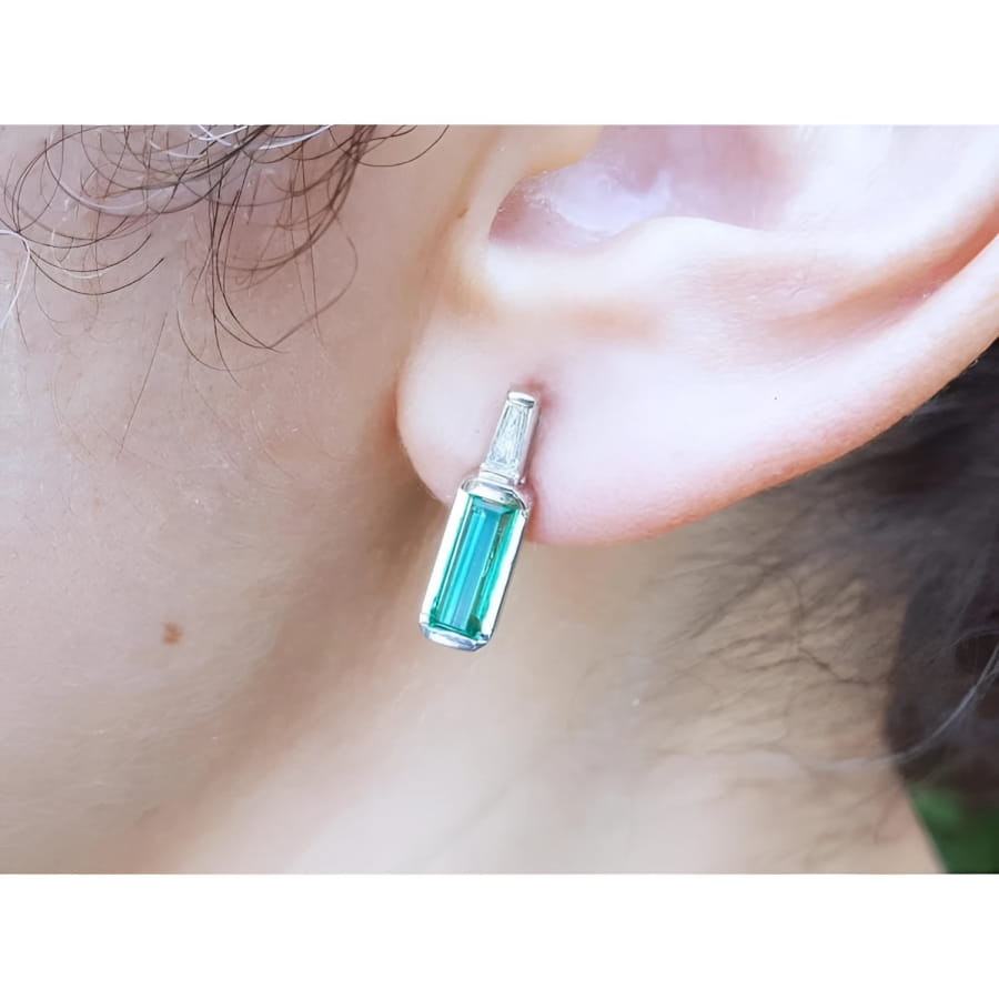Baguette emerald and diamond stud earring in 14k white gold, worn on an ear.