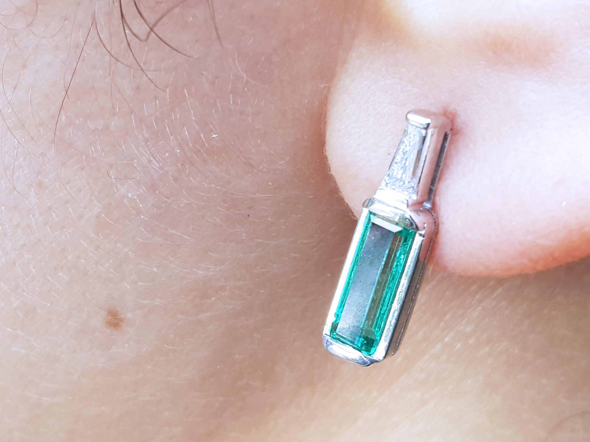 Close-up of a baguette cut emerald stud earring on a person's ear.