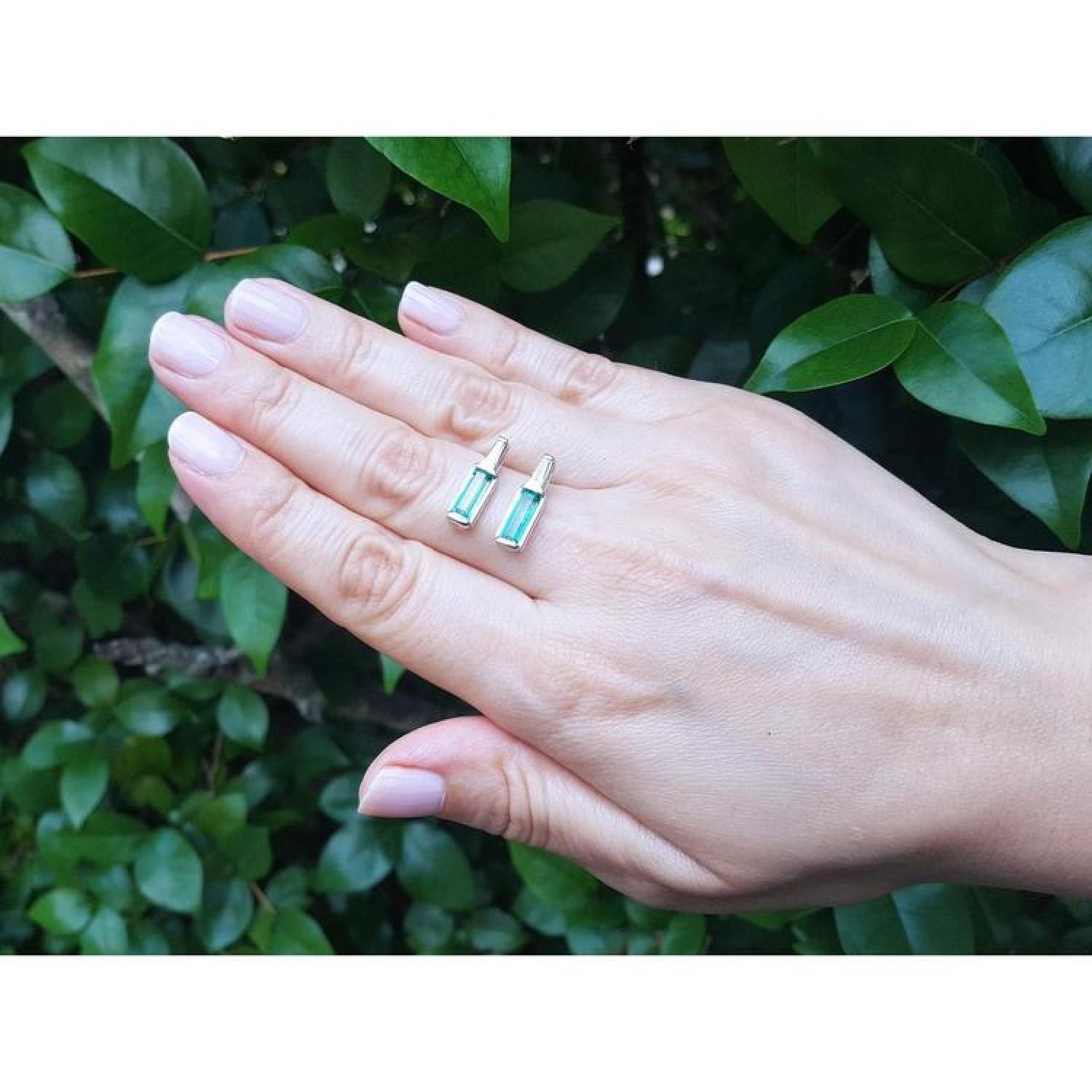 2.00 ct. natural baguette emerald stud earrings in 14k white gold, worn on a hand.