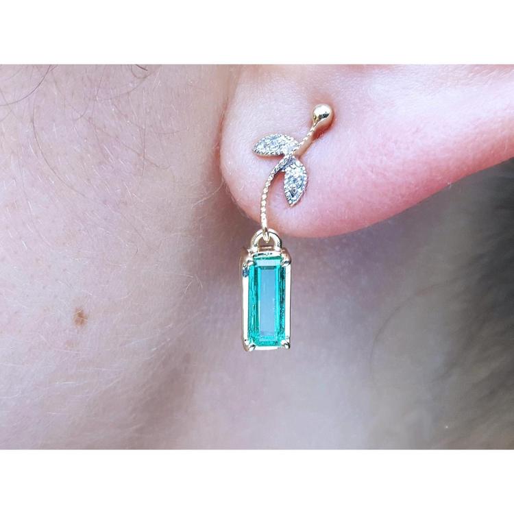 Close-up of dangle colombian emerald earring in 14k yellow gold on a person's ear.