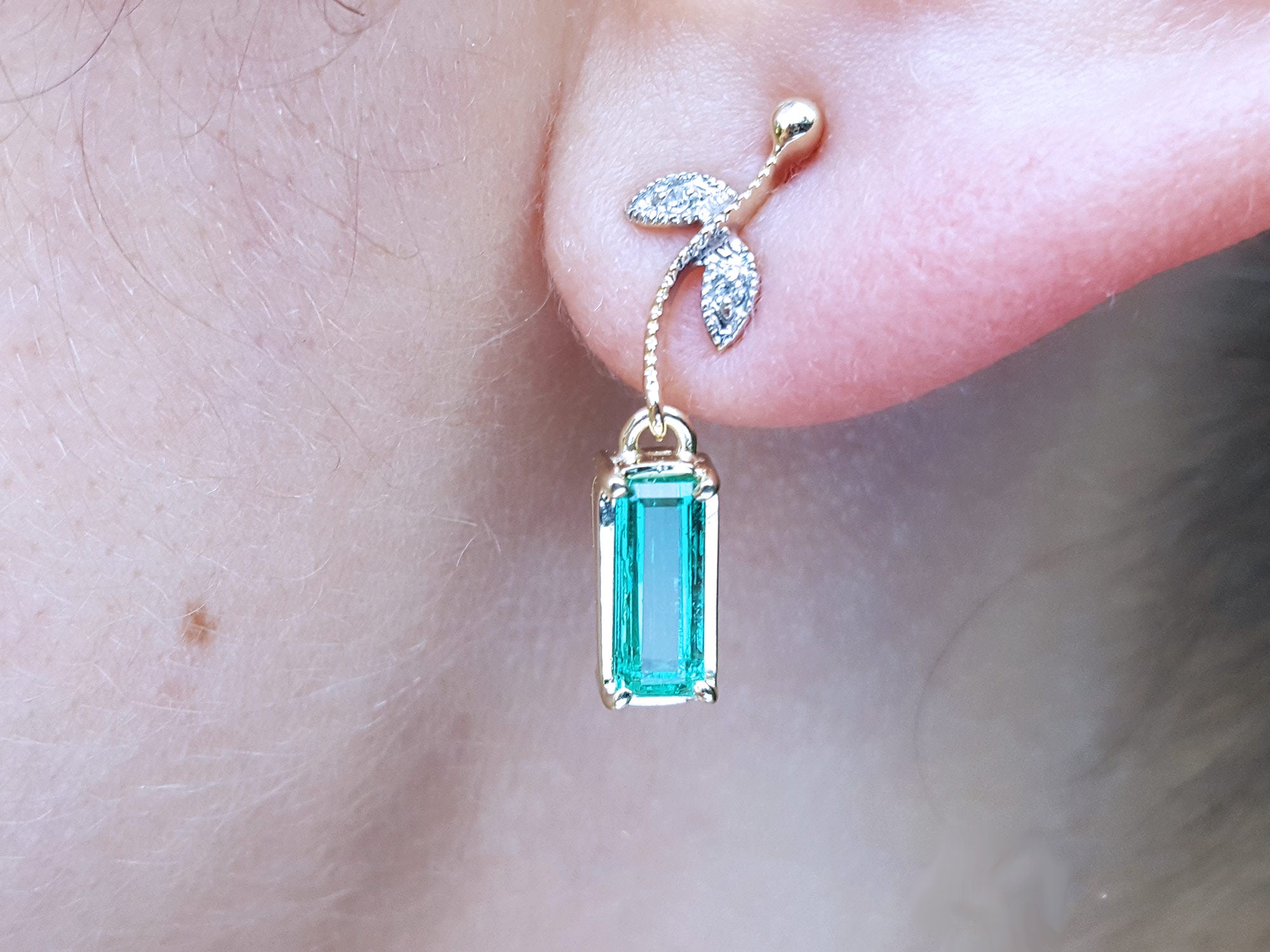 Close-up of dangle emerald earrings yellow gold on a person's ear.