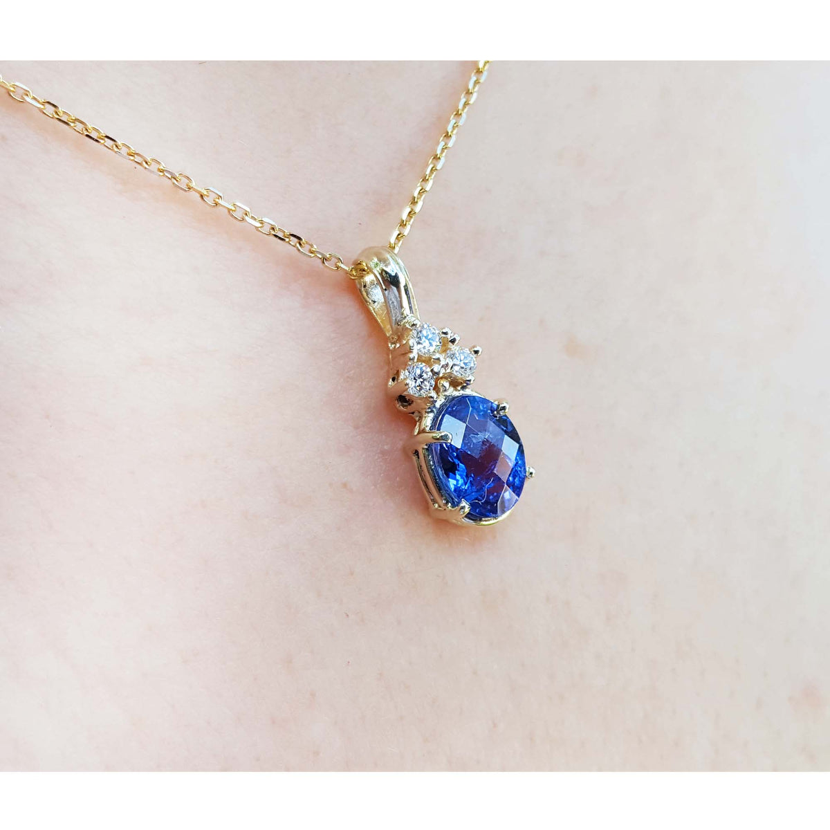 Gold necklace with a tanzanite and diamonds pendant on a light skin background,