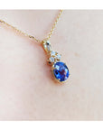 Gold necklace with a tanzanite and diamonds pendant on a light skin background,