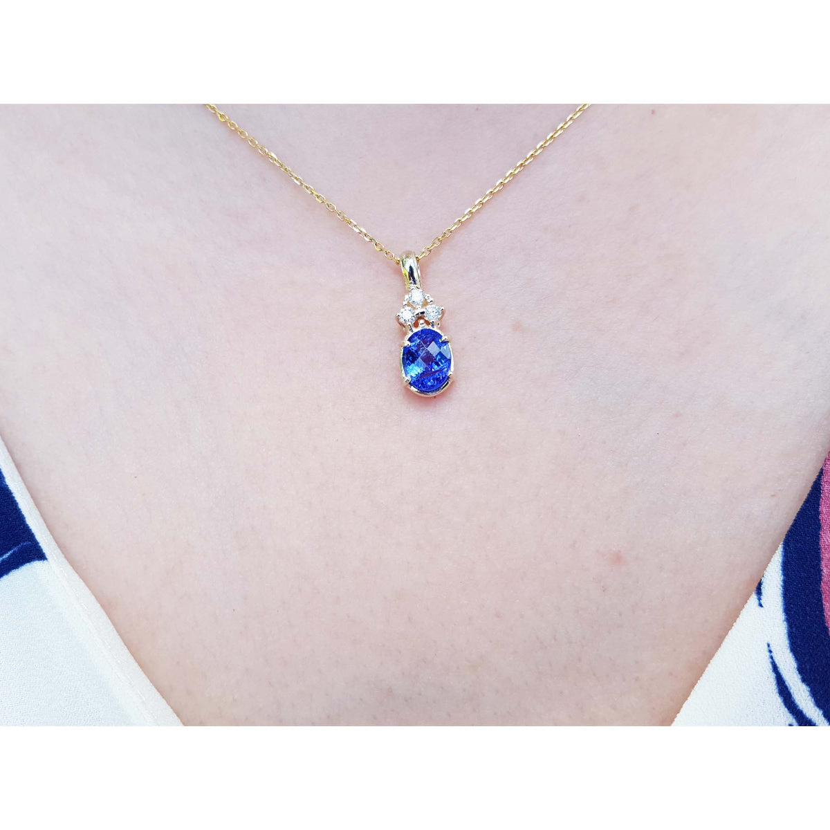 Gold necklace with a natural oval cut tanzanite and diamonds pendant on a person's neck.