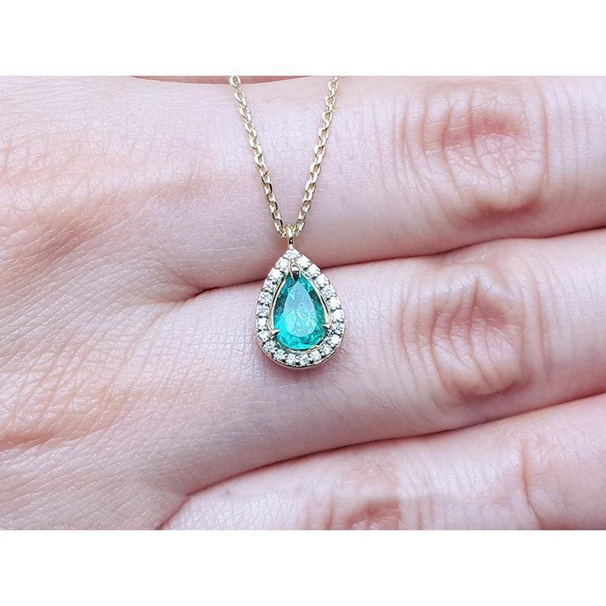 Pear-shaped natural emerald necklace with diamond halo in 14K yellow gold.