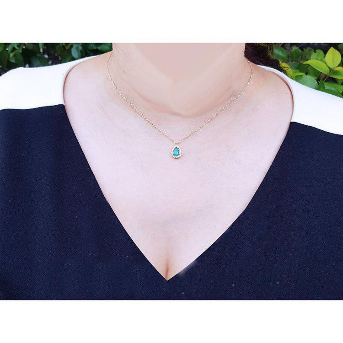 Pear-shaped natural emerald necklace with diamond halo, 14K yellow gold, worn on a woman.