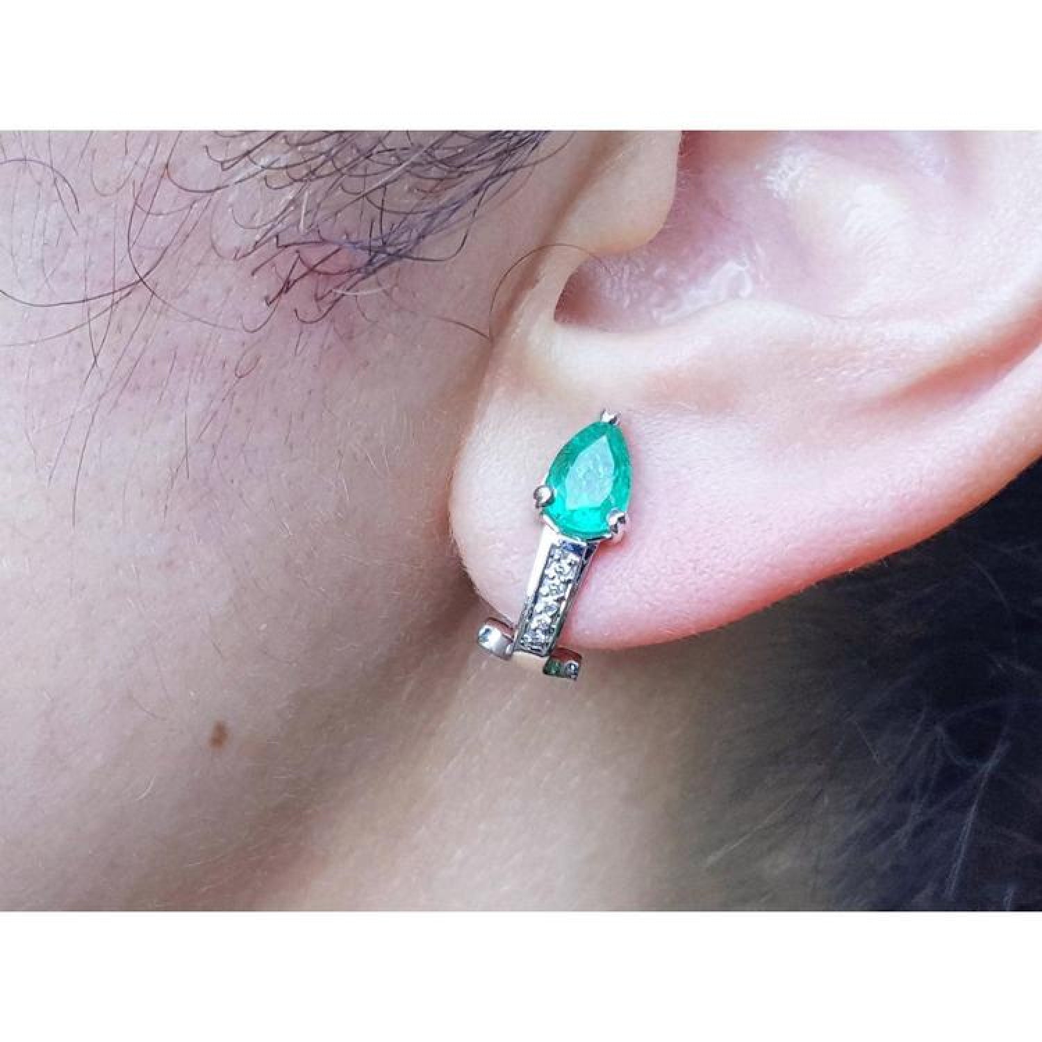 Pear-shaped emerald clip-on earring with accent diamonds in 14K white gold, worn on an ear.