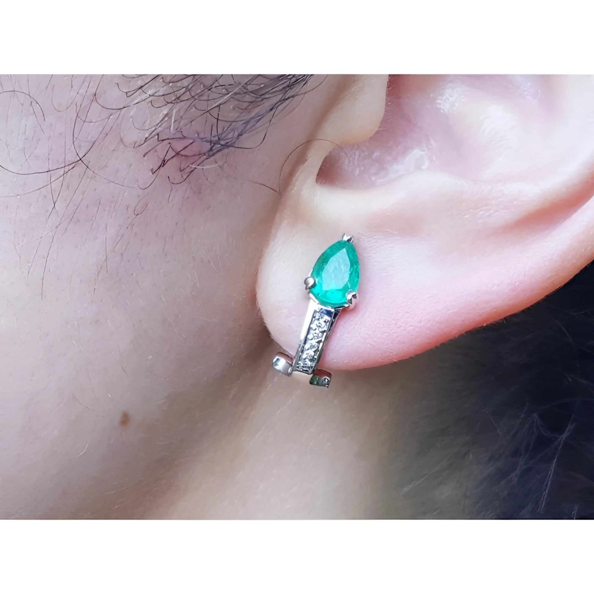 Pear-shaped emerald clip-on earring with accent diamonds in 14K white gold, worn on an ear.