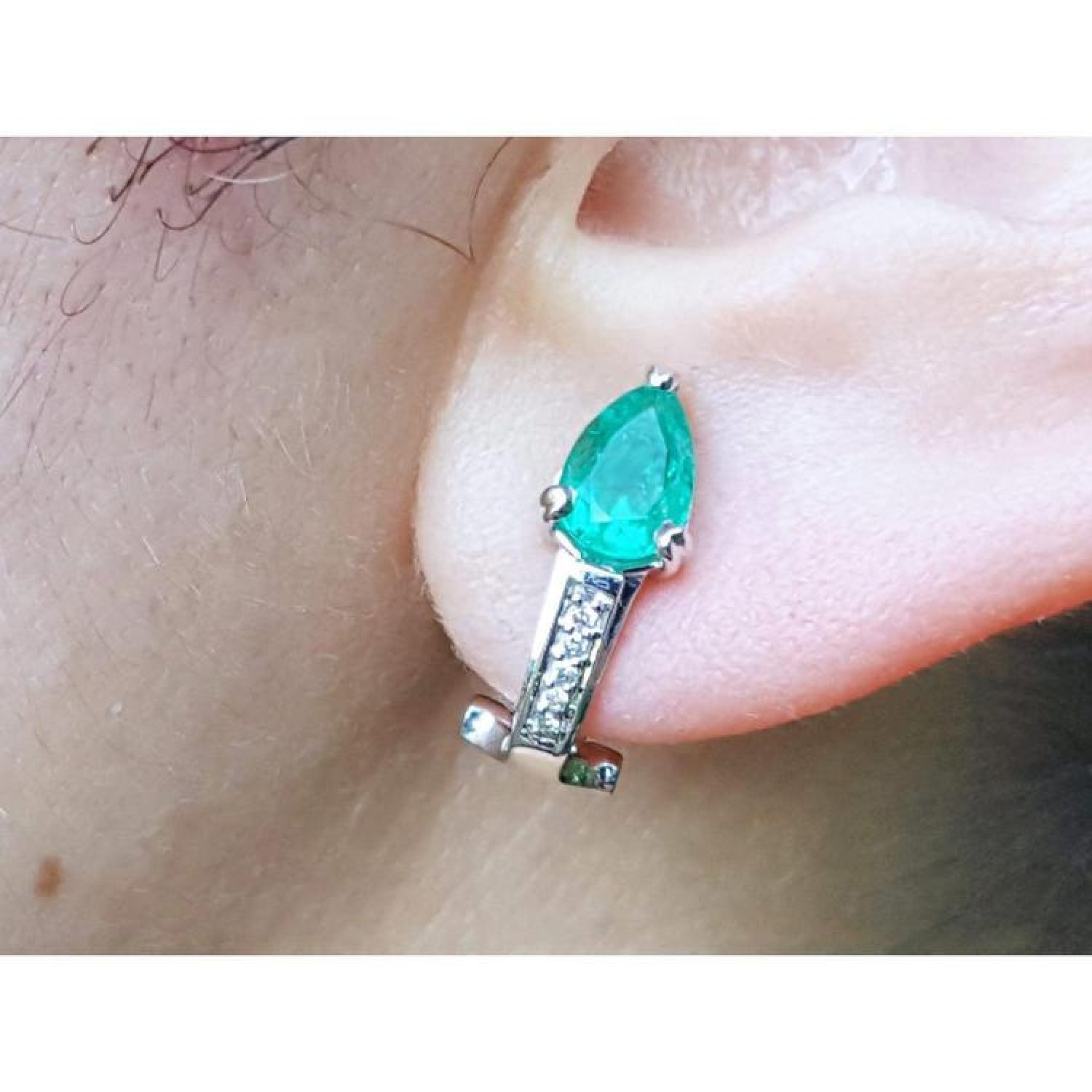 Pear-shaped emerald clip-on earring with accent diamonds in 14K white gold on an ear.