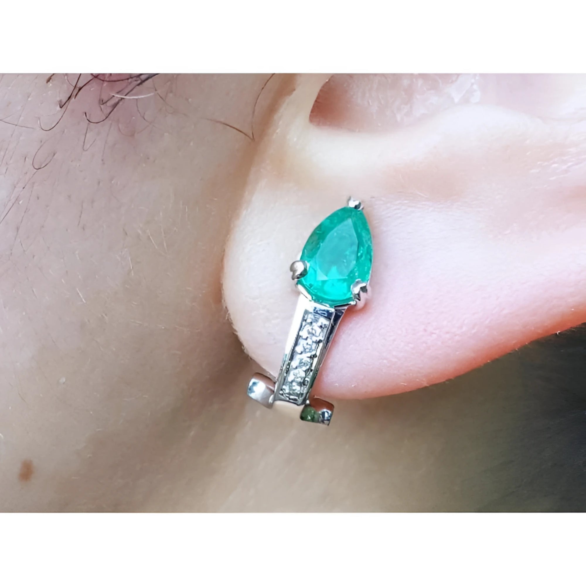 Pear-shaped emerald clip-on earring with accent diamonds in 14K white gold on an ear.
