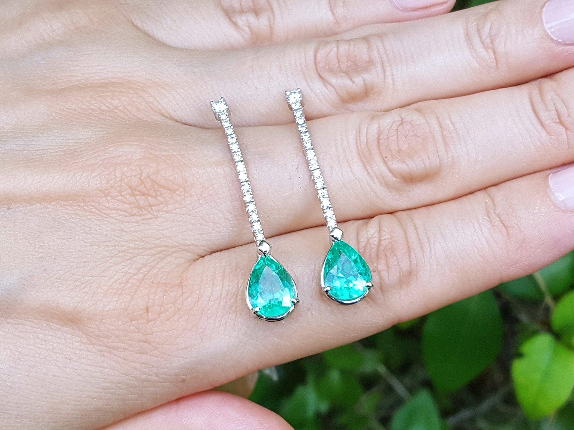 Green teardrop earrings held between fingers with a blurred natural background