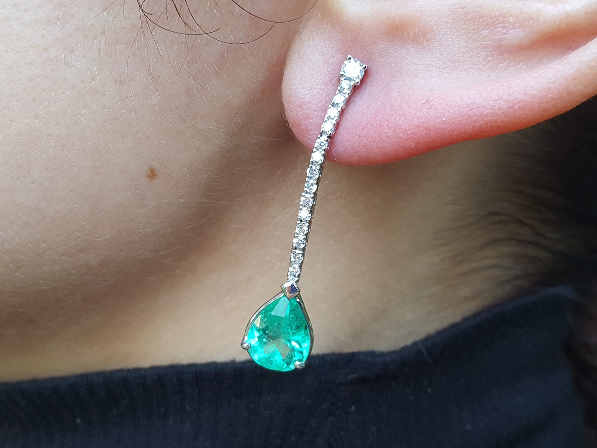 Close-up of a green teardrop earring with a diamond on an ear.