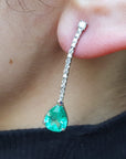 Close-up of a green teardrop earring with a diamond on an ear.