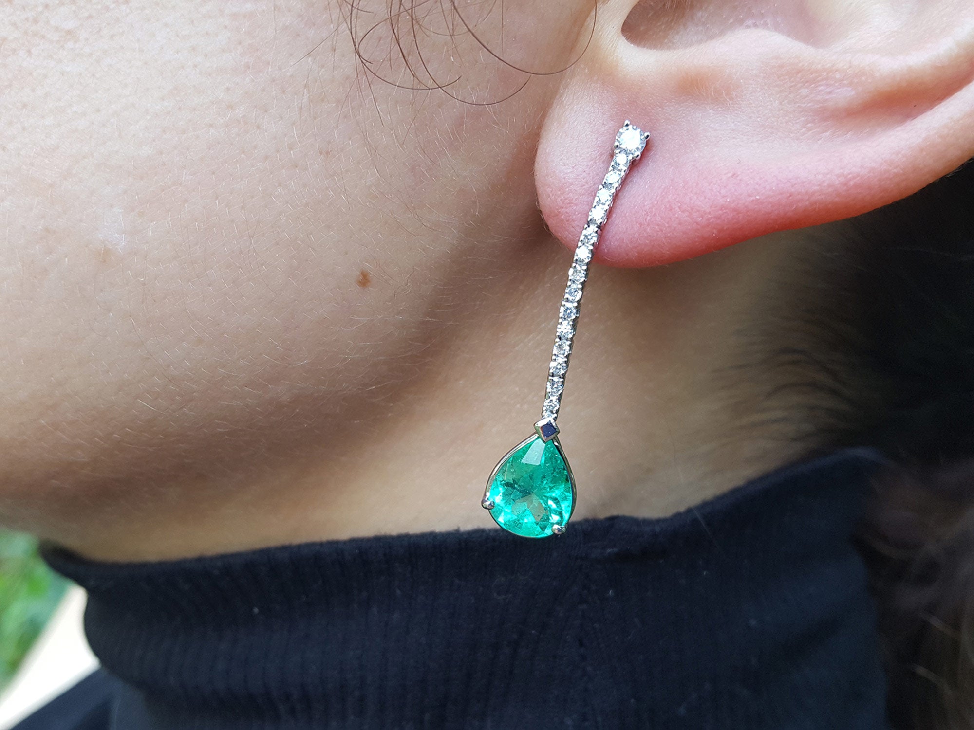 Close-up of a person wearing a green teardrop earring with a blurred background