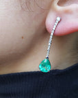 Close-up of a person wearing a green teardrop earring with a blurred background