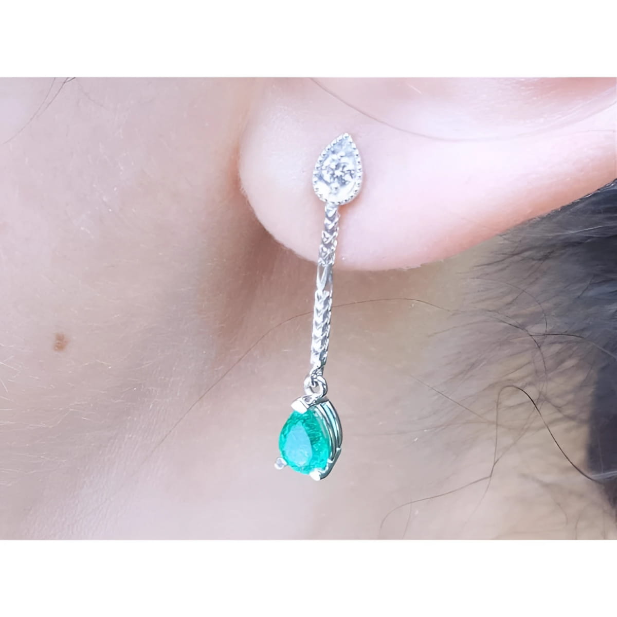 Close-up of a natural emerald teardrop earring with a diamond on a person's ear.