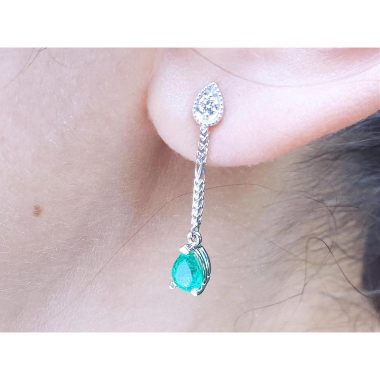 Close-up of an emerald green teardrop earring with a diamond on a person's ear.
