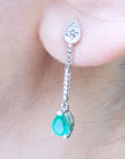 Close-up of an emerald green teardrop earring with a diamond on a person's ear.
