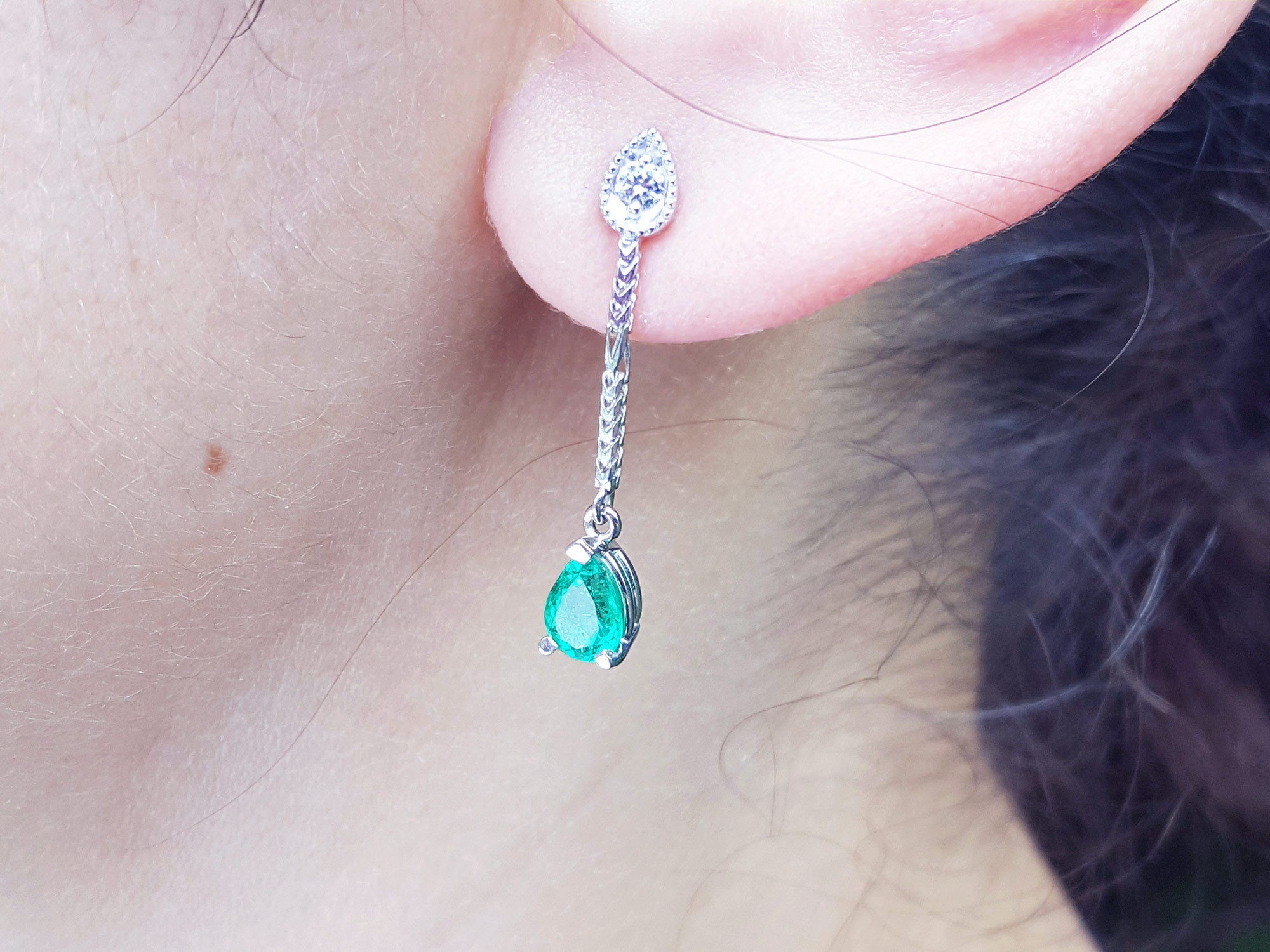 Close-up of a May&#39;s birthstone emerald dangle earring worn by a person.