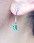 Close-up of a May's birthstone emerald dangle earring worn by a person.