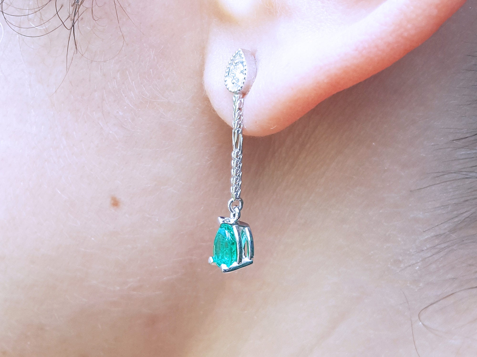 Close-up of a pear shaped dangle earrings worn on an ear.