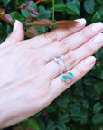 Hand exposing a 14k gold emerald dangle earrings against a green leafy background