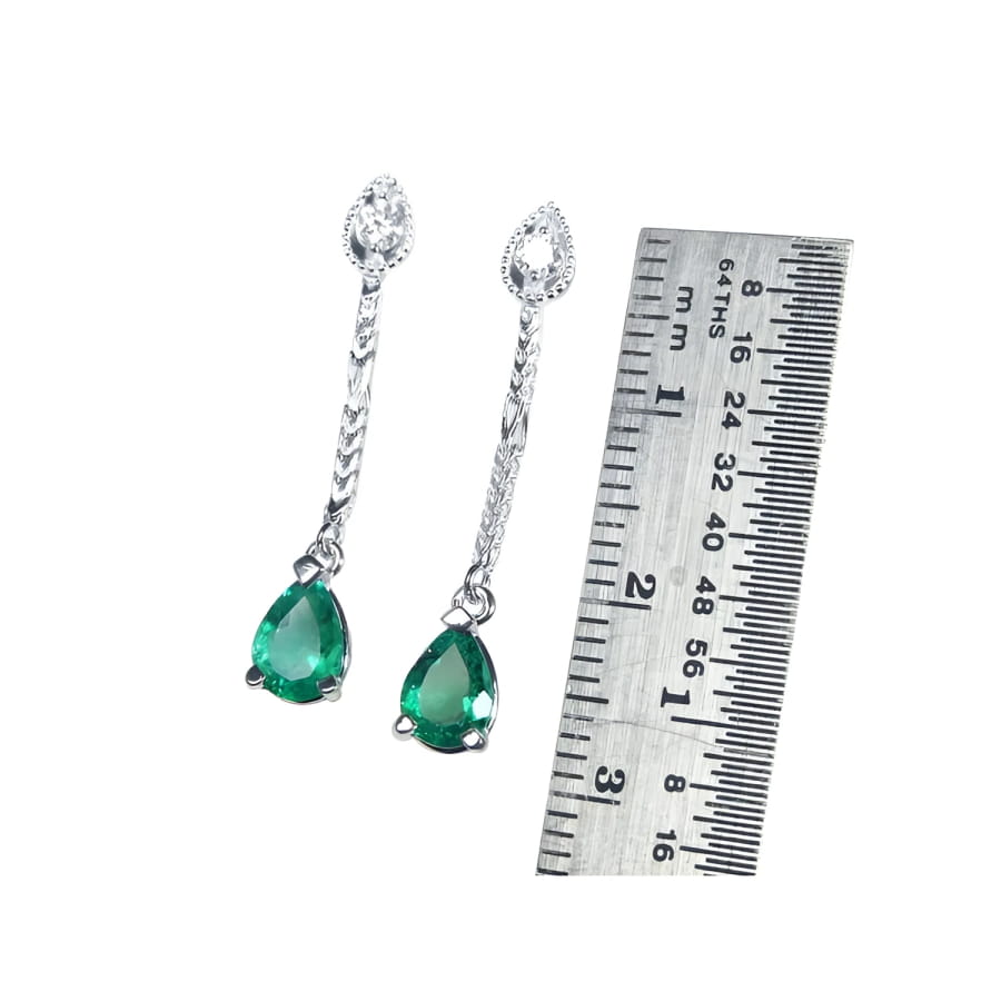 Pear-shaped Muzo Colombian emerald dangle earrings in 14K white gold with diamonds, next to a ruler.
