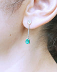 Close-up of woman's ear wearing a teardrop emerald earring with a blurred background
