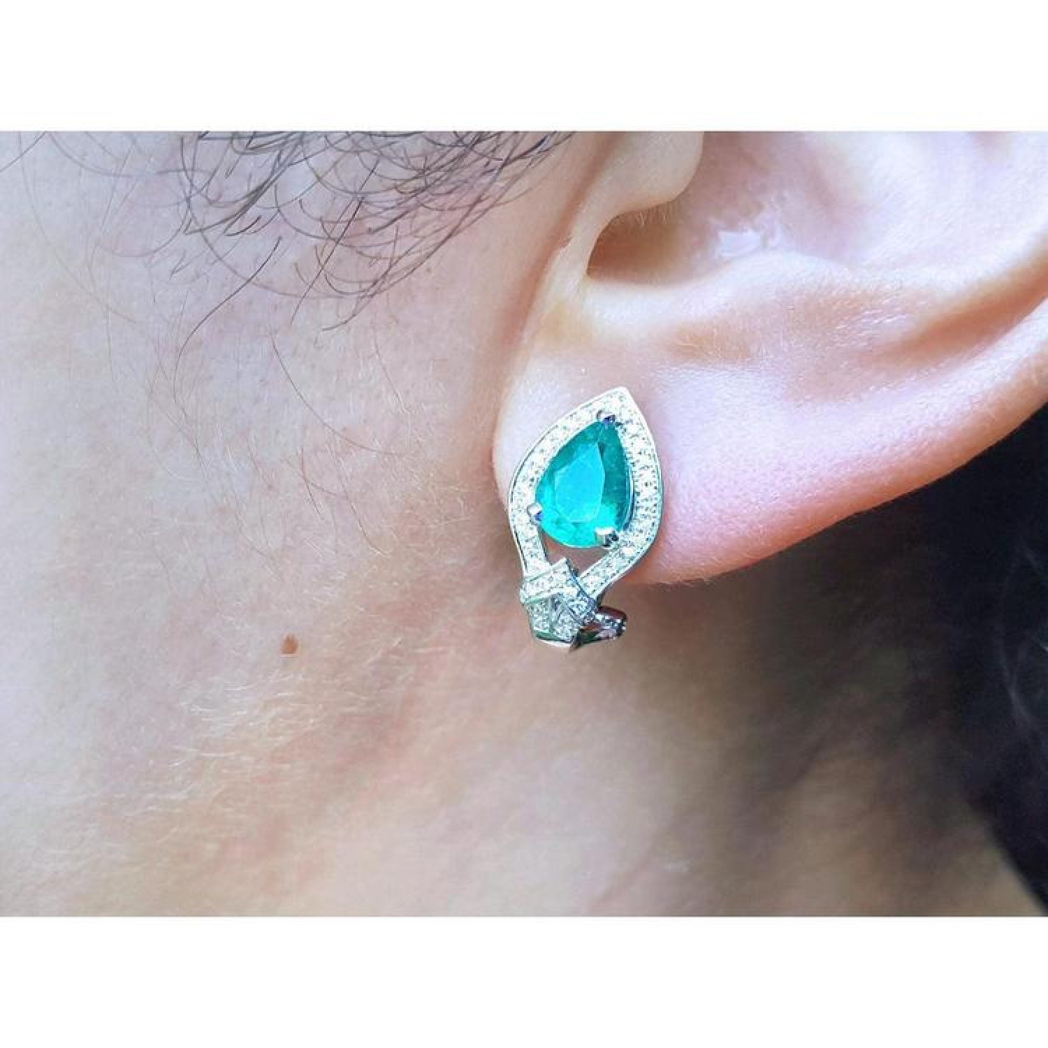 Pear-shaped Colombian emerald and diamond 14K gold clip/post earring on an ear.