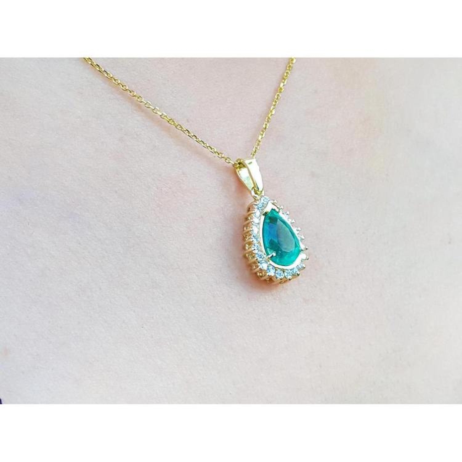 Teardrop emerald pendant with a diamond halo on a gold chain, worn on a woman's neck.