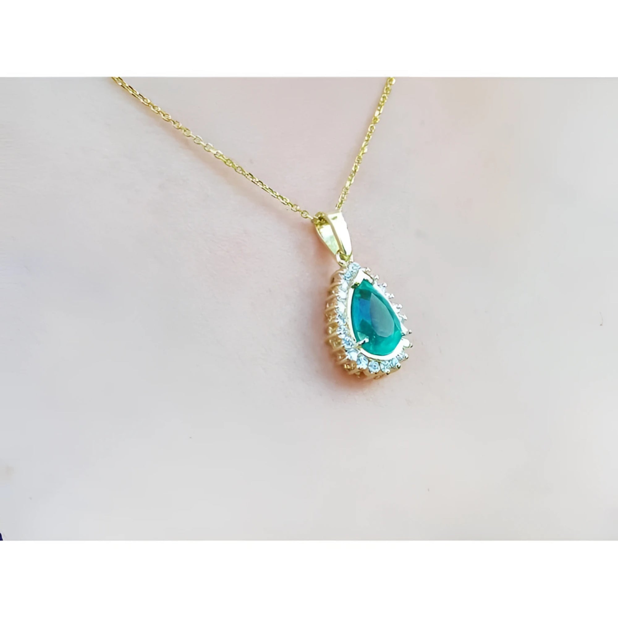 Teardrop emerald pendant with a diamond halo on a gold chain, worn on a woman's neck.