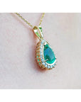 Gold pendant with a natural teardrop-shaped emerald on a light pink skin background.