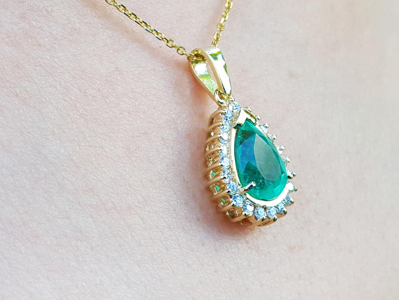 Gold pendant with a teardrop emerald on a light pink skin background