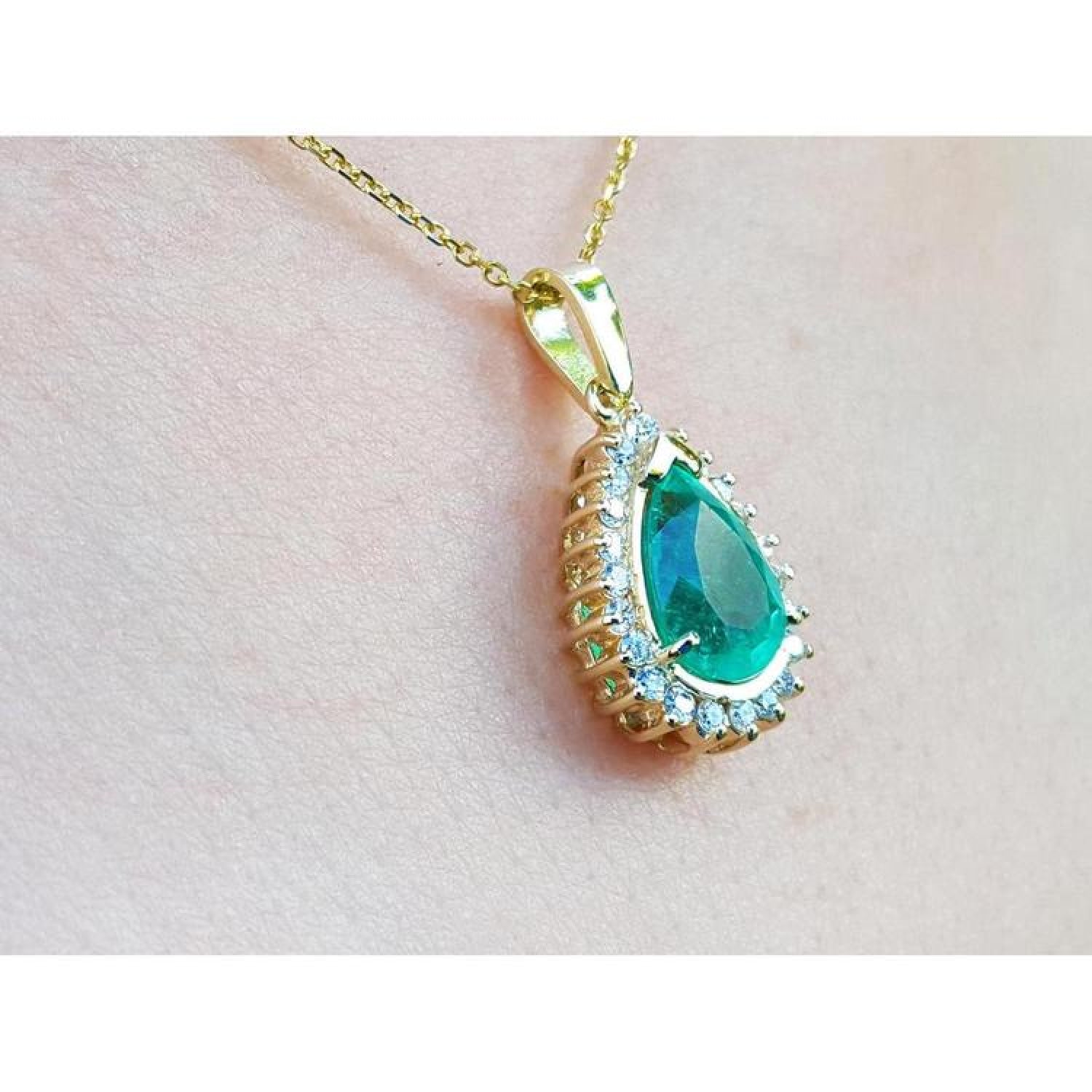 Teardrop emerald pendant with diamond halo on a gold chain, worn on a person.