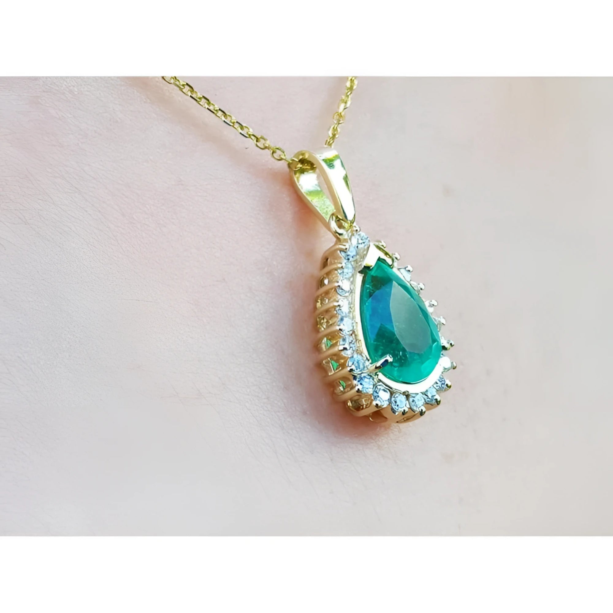 Teardrop emerald pendant with diamond halo on a gold chain, worn on a person.