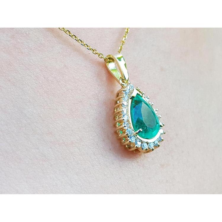 Teardrop emerald pendant with diamond halo on a gold chain, worn on a person.