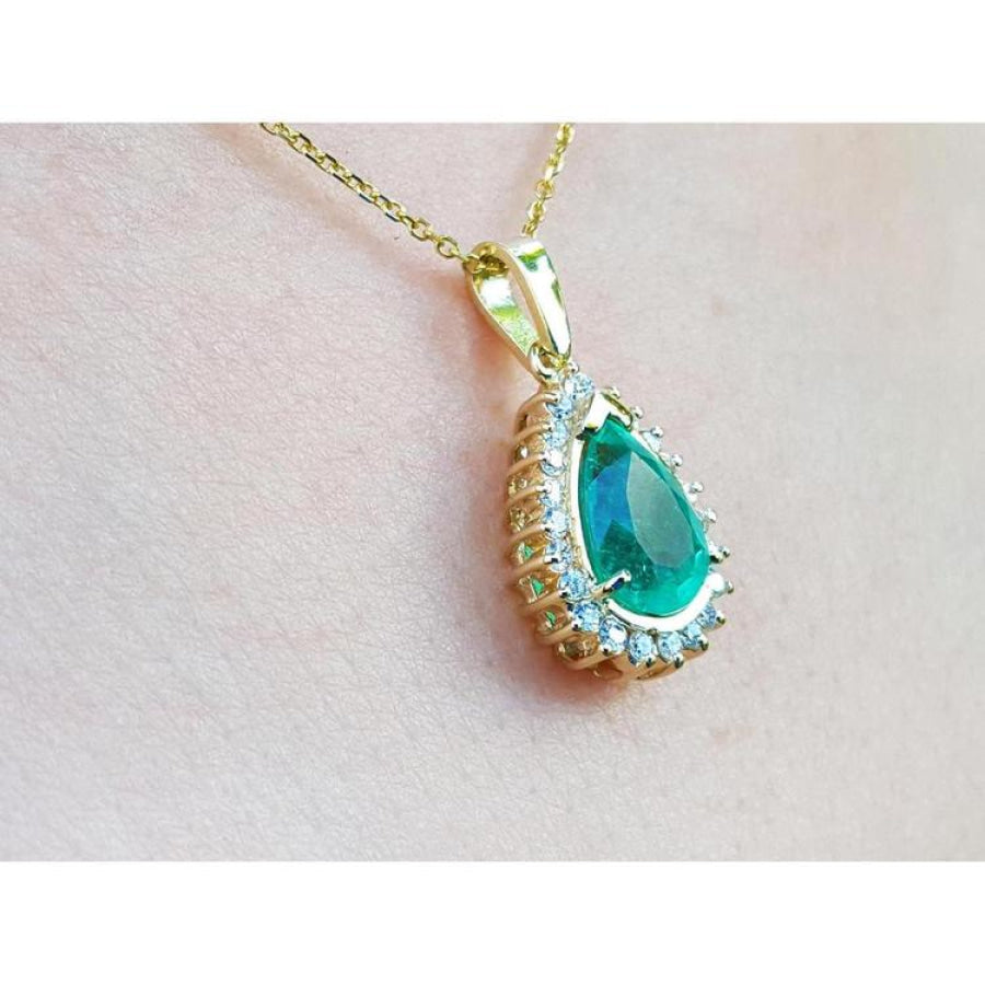 Teardrop emerald pendant with diamond halo on a gold chain, worn on a person.