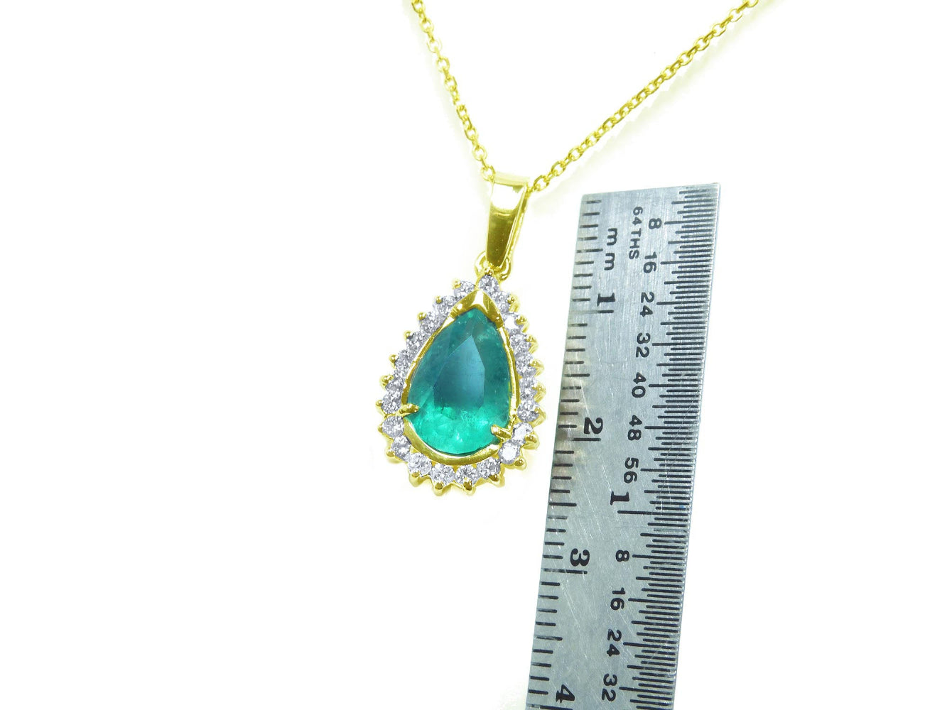 Gold necklace with a natural emerald teardrop pendant next to a ruler for scale on a white background