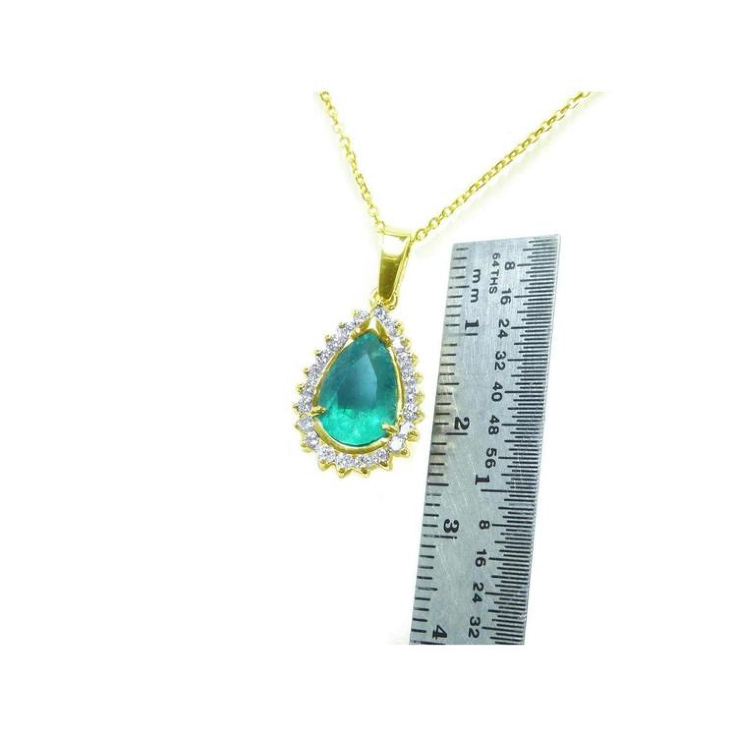 Teardrop Colombian emerald pendant with diamond halo on a gold chain, next to a ruler.
