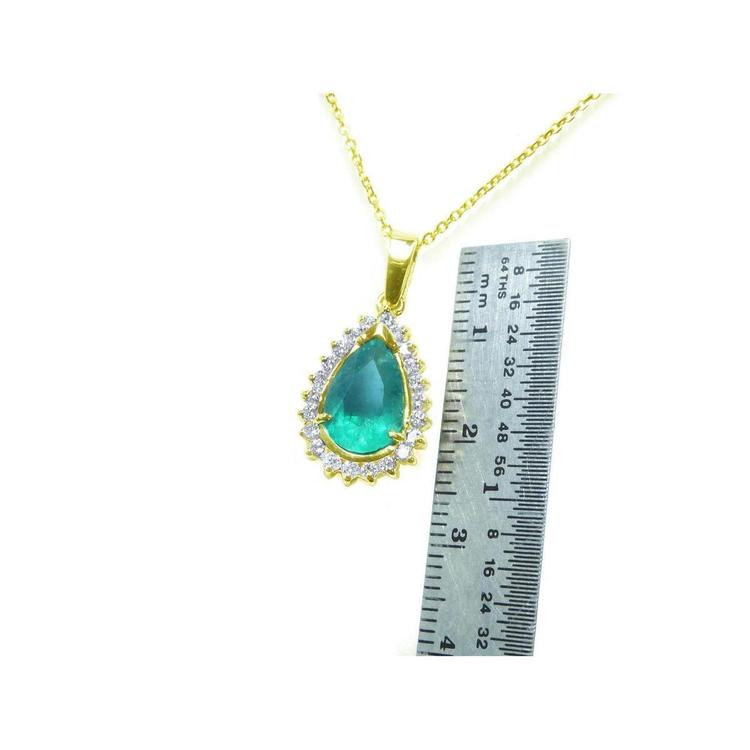 Teardrop Colombian emerald pendant with diamond halo on a gold chain, next to a ruler.